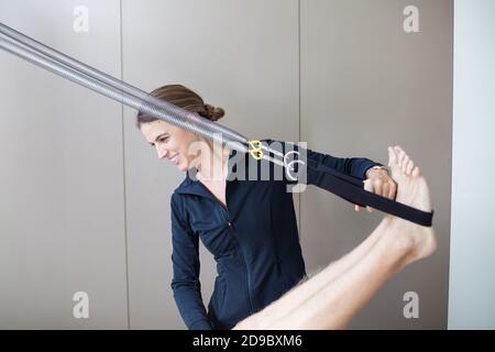Istruttore di pilates femminile che assiste l'uomo irriconoscibile sul riformatore Foto Stock