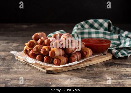 Maiale in coperte. Salsicce avvolte in pancetta affumicata su tavolo di legno Foto Stock