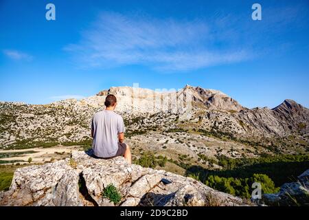 Giovane uomo di viaggio seduto sulla roccia nelle montagne di Maiorca Serra de Tramuntana e guardando al monte maggiore Puig, posto per il testo Foto Stock