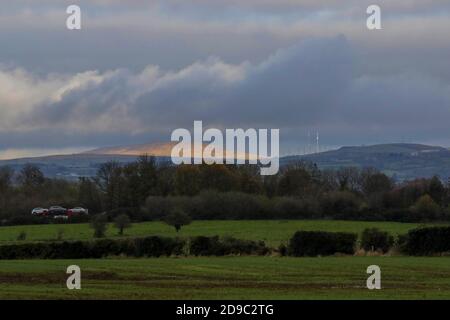 Moira, County Down, Irlanda del Nord. 04 Nov 2020. Tempo nel Regno Unito - dopo una mattinata di sole, si è verificata una giornata con nuvole grigie. Una giornata tranquilla con poco vento ma colori autunnali in mostra. Un'esplosione di luce solare illumina le colline di Belfast in lontananza in un grigio pomeriggio d'autunno. Credit: CAZIMB/Alamy Live News. Foto Stock