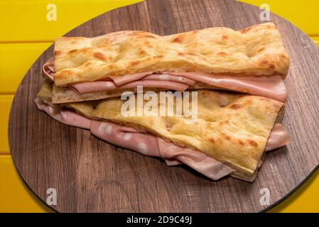 due focaccia panino ripieno di mortadella bolognese su legno tagliere e sfondo giallo Foto Stock