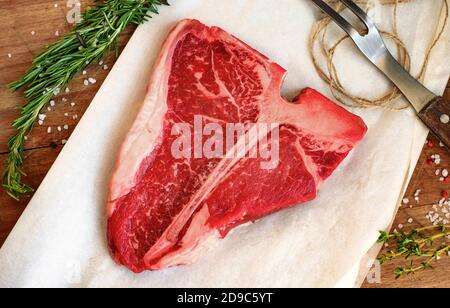 la bistecca di porterhouse cruda con erbe e sale è sul Carta su una tavola di legno Foto Stock