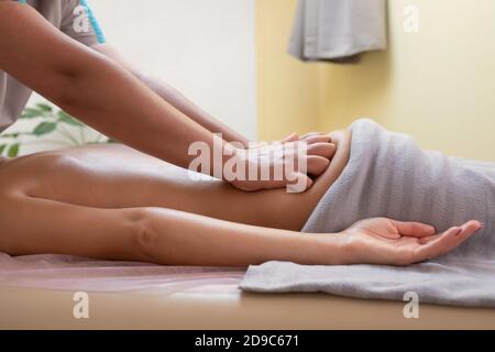 Mani di terapeuta femminile sfregamento loin di cliente femminile durante sessione di massaggio Foto Stock