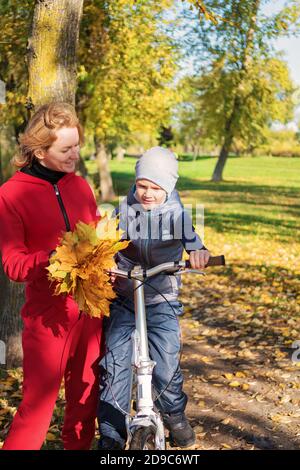 Felice famiglia madre e figlio comunicare in una passeggiata autunno. Madre insegna a suo figlio di andare in bicicletta. Foto Stock