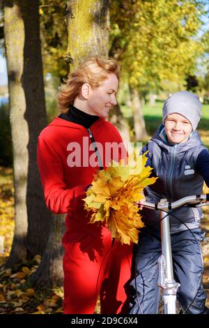 Felice famiglia madre e figlio comunicare in una passeggiata autunno. Madre insegna a suo figlio di andare in bicicletta. Foto Stock