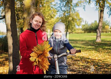 Felice famiglia madre e figlio comunicare in una passeggiata autunno. Madre insegna a suo figlio di andare in bicicletta. Foto Stock