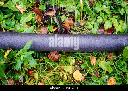 Primo piano di tubi in plastica nera con geotessile sdraiato sul erba Foto Stock