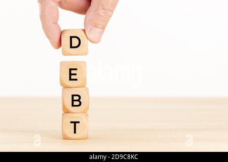 Concetto di debito. Mano che tiene una pila di blocchi di legno sul tavolo. Sfondo bianco. Spazio di copia Foto Stock