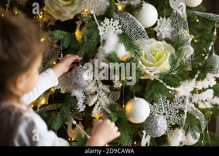 Una bambina raggiunge per un giocattolo dell'albero di Natale con la sua mano. Decorazioni natalizie, in attesa di una vacanza e di un miracolo. Anno nuovo. Bianco, rosa e blu dec Foto Stock