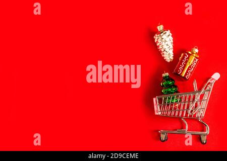 Un cestino pieno della spesa di vetro diverso e giocattoli lucidi dell'albero di Natale su uno sfondo rosso. I giocattoli di Natale vengono fuoriuscite dal cestino del negozio Foto Stock