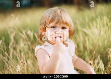 la bambina si siede all'aperto e tiene un dito nel suo bocca Foto Stock