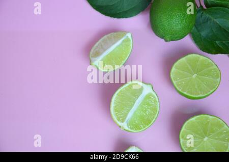 Sfondo da una fetta di frutti di lime interi con foglie su sfondo rosa. Per fare una bevanda di limonata, tè, cocktail, mojito, detox. Foto Stock