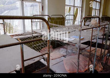 Letti per bambini in un asilo abbandonato. L'interno di un locale in uno degli edifici della zona di esclusione radioattiva di Chernobyl. Foto Stock