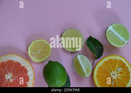 Lay piatto di agrumi come lime e limone con limone lascia sulla luce sfondo rosa facendo un telaio Foto Stock