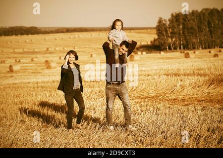 Felice giovane famiglia con due anni bambina a piedi in campo raccolto Foto Stock