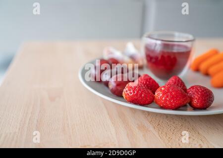 Piatto di frutta frutta sana per colazione su tavolo di legno. Fragole, succo di mirtilli detox, uva. Cibo di colore rosso Foto Stock