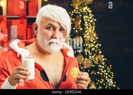 Biglietto di auguri natalizi. Latte e biscotti per Babbo Natale. Santa divertente. Babbo Natale. Ritratto di Santa con biscotti al cioccolato e bicchiere di latte. Foto Stock