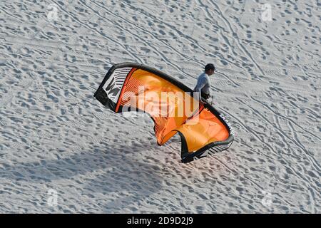 uomo che cammina sulla spiaggia con aquilone di parasurf arancione Foto Stock