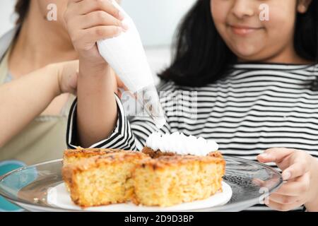 Primo piano delle mani della ragazza ispanica che decorano una torta con Panna montata - Latina madre e figlia decorazione una torta Foto Stock