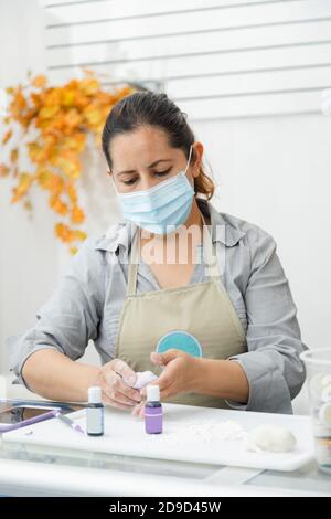 Pasticciere lavorando con fondente per decorare una torta - Donna cucina con maschera - Donna pittura argilla con coloranti Foto Stock