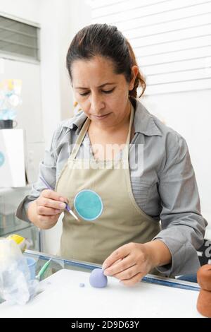 Donna ispanica che lavora nella sua pasticceria - donna Latina lavorare con fondente per decorare una torta - pasticceria imprenditore chef - donna che fa mestiere con Foto Stock