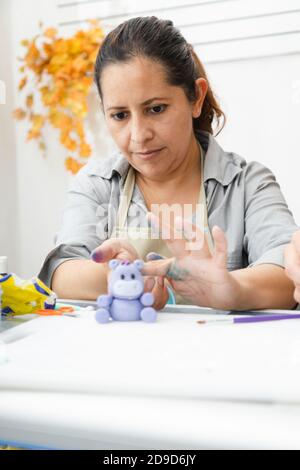 Donna ispanica che lavora nella sua pasticceria - donna Latina lavorare con fondente per decorare una torta - pasticceria imprenditore chef - donna che fa mestiere con Foto Stock