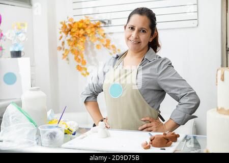 Donna latina orgogliosa nella sua pasticceria - donna con grembiule che guarda la macchina fotografica nel suo laboratorio di torta - intraprendente Donna ispanica Foto Stock