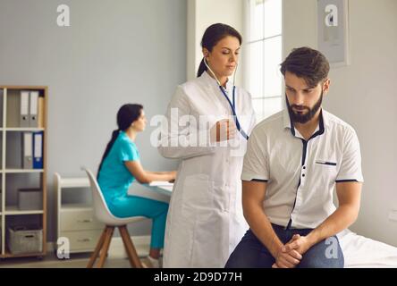 Dottore femminile in uniforme ascolto del respiro di un giovane maschio paziente attraverso stetoscopio Foto Stock