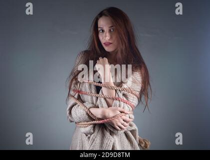 Immagine di giovane donna inbinata con corda sul maglione sfondo grigio Foto Stock