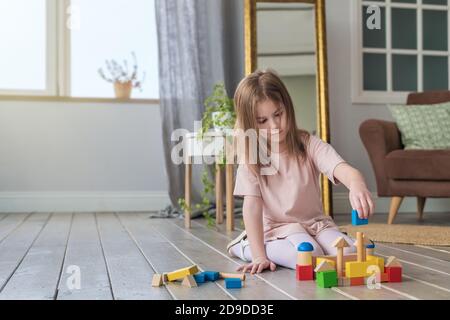 Cute ragazza gioca sul pavimento con un costruttore di legno Foto Stock