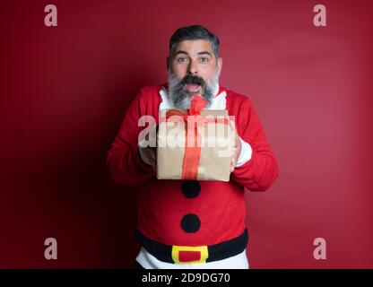 Ritratto di uomo bearded stupito che indossa un maglione di babbo natale, tiene un grande pacchetto che riceve nella celebrazione di Natale, grida wow che si sente intereste Foto Stock