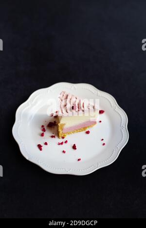 Una fetta di deliziosa cheesecake di lamponi decorata con lamponi liofilizzati su un piatto bianco si erge su uno sfondo scuro, vista dall'alto Foto Stock