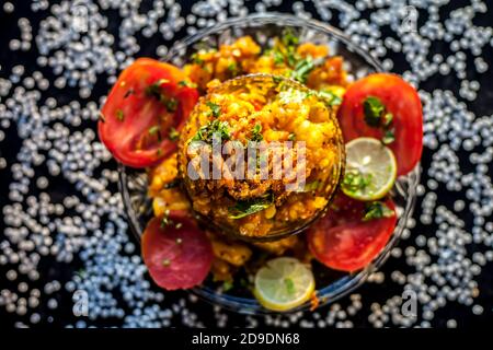 Primo piano di piccante saporito sabudana khichdi o sago palla khichdi insieme con alcuni pomodori a fette, alcuni limoni tagliati in un piatto di vetro, e il salo crudo bal Foto Stock