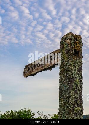 Un vecchio palo di legno di segno coperto con Lichens che punta il Direzione Lennoxtown Foto Stock