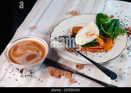 Colazione sana con uova in camicia su pane tostato con foglie di insalata verde. Tuorlo d'uovo spalmato Foto Stock