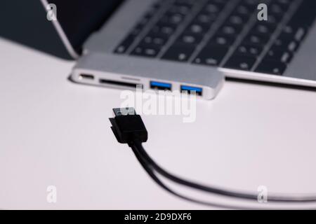 le foto supermacro concentrate su un cavo usb a nero, un adattatore usb-usb-c e un computer portatile sono decisamente fuori fuoco Foto Stock