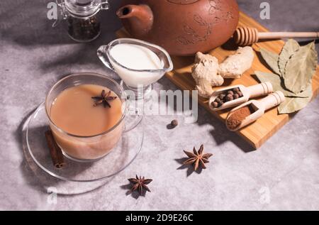 Una tazza di tè caldo indiano masala tè, caraffa di latte, teiera e spezie su uno sfondo grigio. Orientamento orizzontale. Foto Stock