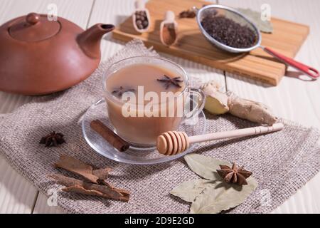 Tè Masala-tè indiano rinvigorente con latte e spezie su sfondo grigio in una tazza di vetro e una teiera in ceramica. Orientamento orizzontale. Foto Stock