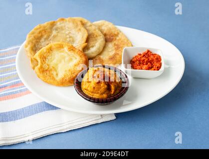 Tortillas puri fritte indiane con tapas vegetali su un piatto ovale bianco. Stoviglie tovagliolo a righe sotto il piatto. Sfondo blu. Foto Stock