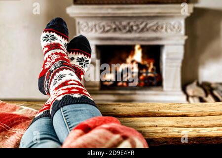 Calze natalizie in lana e gambe donna su tavolo di legno. Spazio per la vostra decorazione. Caminetto all'interno della casa con una calda luce arancione di Fire.Copy spazio Foto Stock