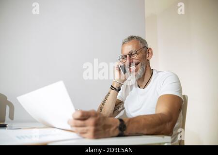 Un adulto sorridente che parla al telefono per quanto riguarda il business paper Foto Stock