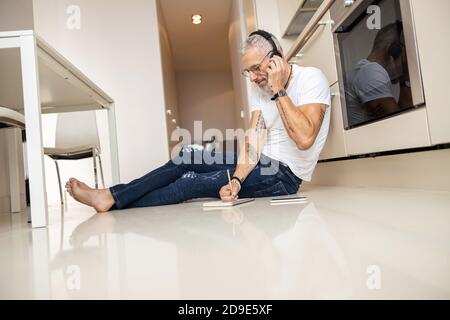 Uomo che parla con l'auricolare e che scrive nel blocco note Foto Stock