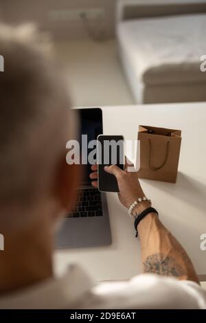 Uomo che fa clic sul suo smartphone vicino a una borsa marrone Foto Stock