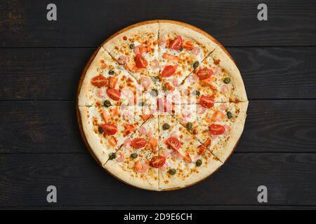 Pizza con gamberetti, salmone, pomodoro e capperi su tavola di legno Foto Stock