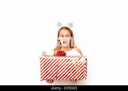 Bella ragazza di capretto sorpresa che tiene una scatola di regalo a strisce rosse di Natale con un nastro e un arco nelle sue mani. Ci sono fiocchi di neve sulla testa. Isolato Foto Stock