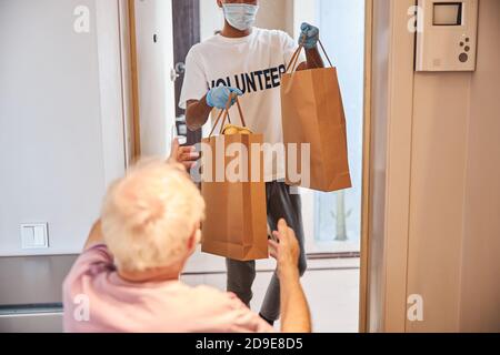 Caregiver in guanti di lattice che danno i prodotti alimentari ad un pensionato solitario Foto Stock