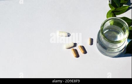 Tazza di vetro con acqua e capsule e pilli su fondo bianco. Il tema della medicina nutraceutica e l'assunzione di integratori biologici. Foto Stock