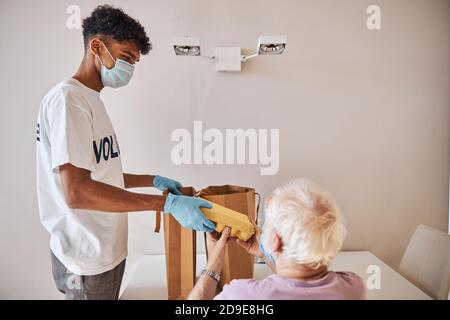 Giovane volontario che consegna i prodotti alimentari ad un pensionato Foto Stock