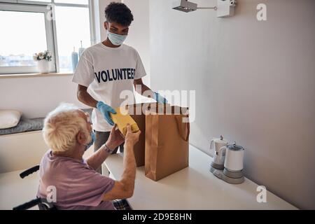 Uomo in sedia a rotelle che prende cibo dal volontario Foto Stock