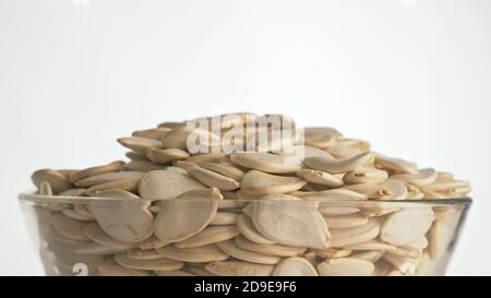 I dadi con la buccia semi di zucca sono ruotare su di una tavola in una piastra. Snack nel piatto trasparente isolato su un sfondo bianco sono la filatura in movimento. Foto Stock